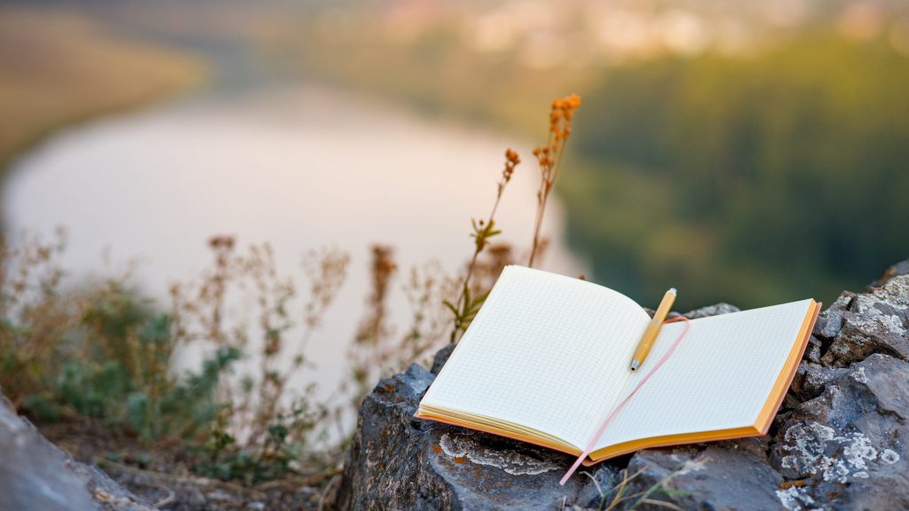 an open empty book with a fountain pen outdoors, the background is a blurred river and forest. a writer in search of inspiration in nature